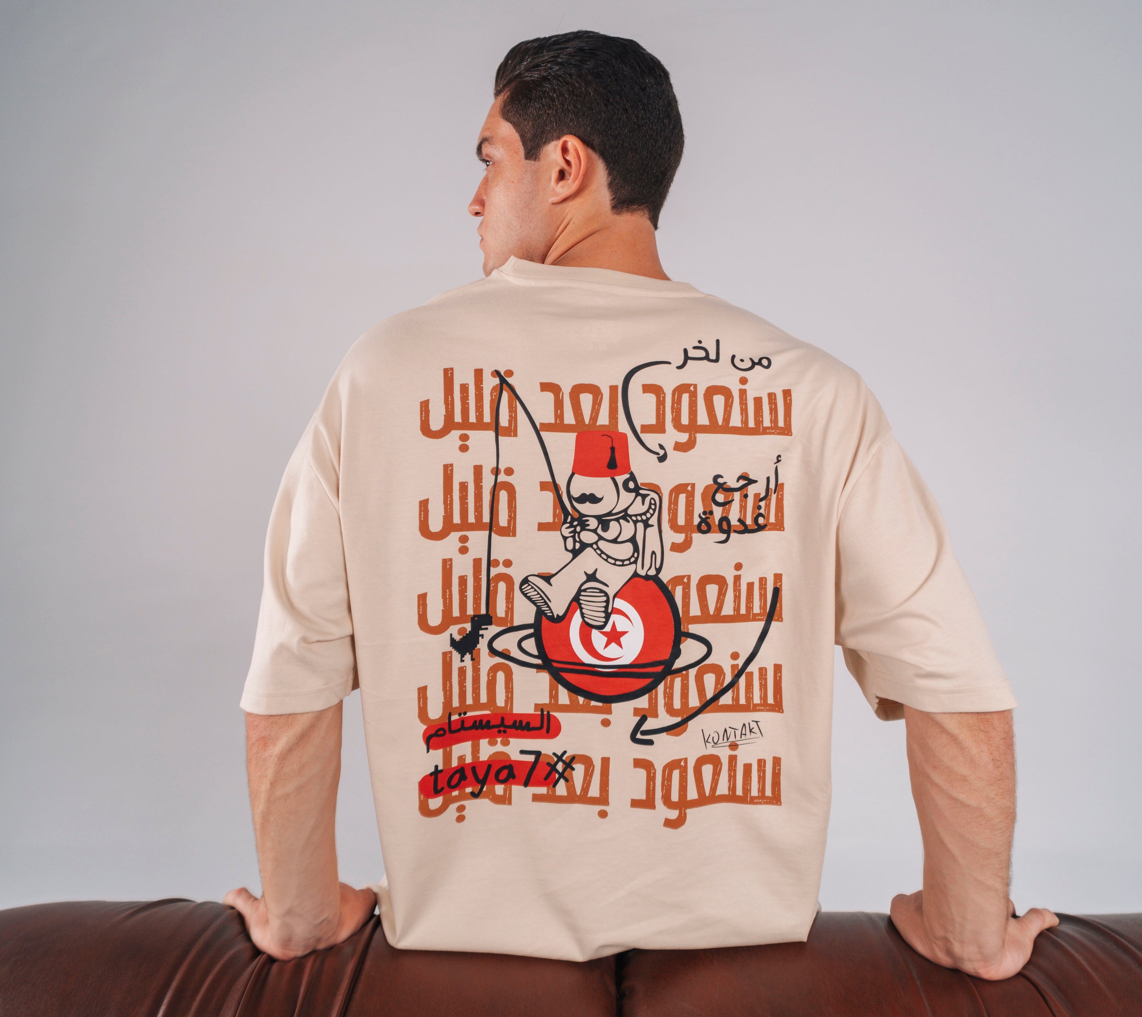 Deux mannequins portent des t-shirts unisexes KONTAKT noirs, dont un modèle avec un imprimé graphique inspiré de la presse tunisienne, photographiés en studio devant un décor de journaux