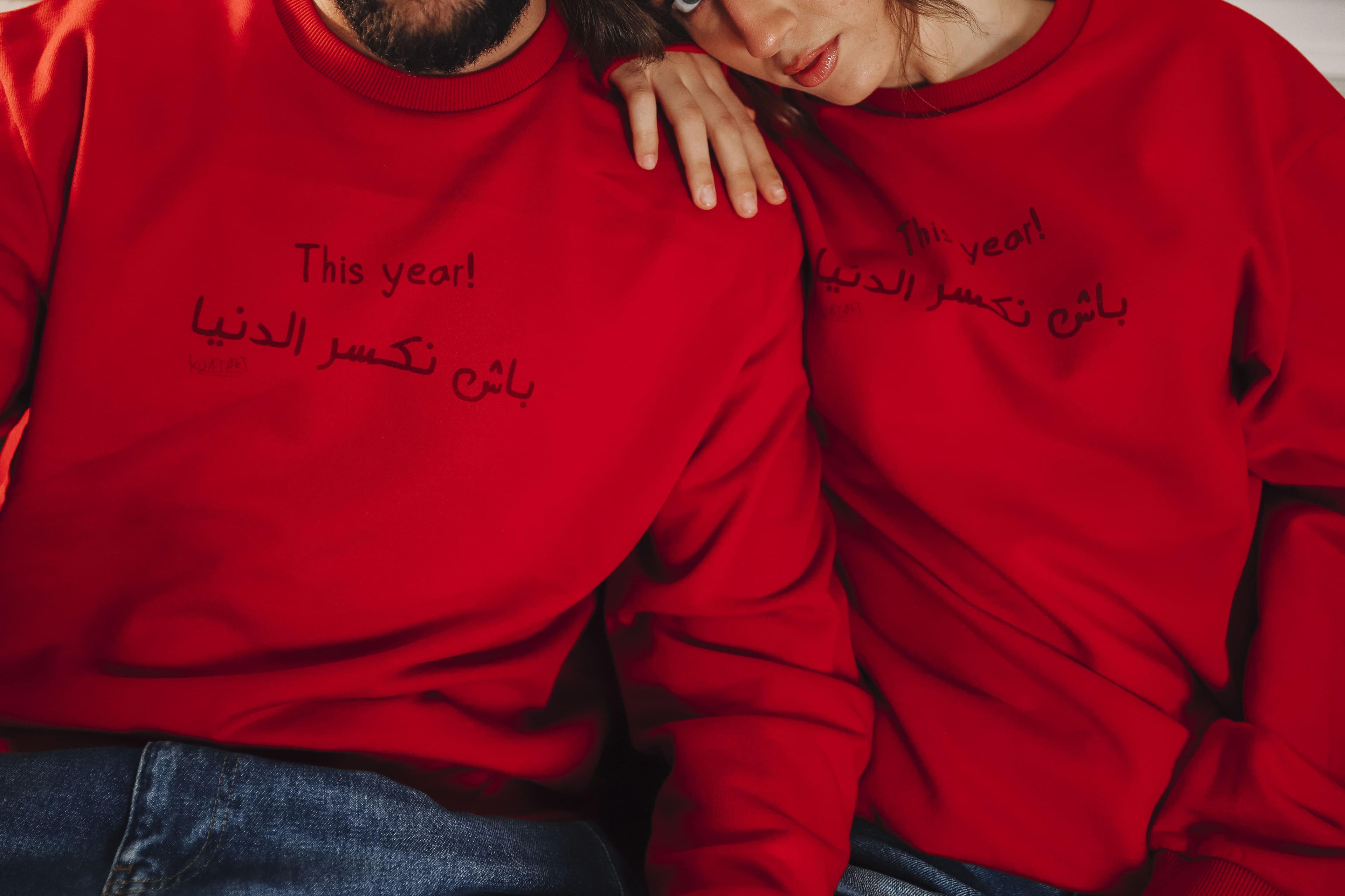 Deux mannequins portent des sweats unisexes KONTAKT rouges avec message typographique en arabe et en anglais, photographiés en studio